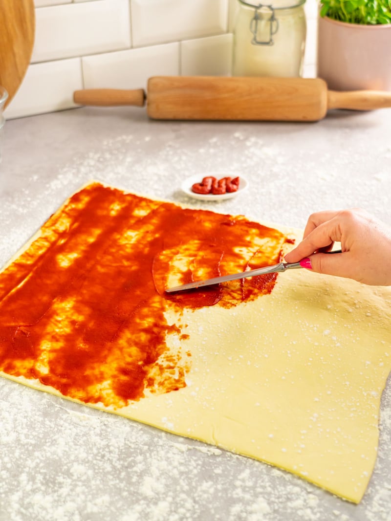 Dieses Bild zeigt wie der Pizzateig mit Tomatensoße bestrichen wird.