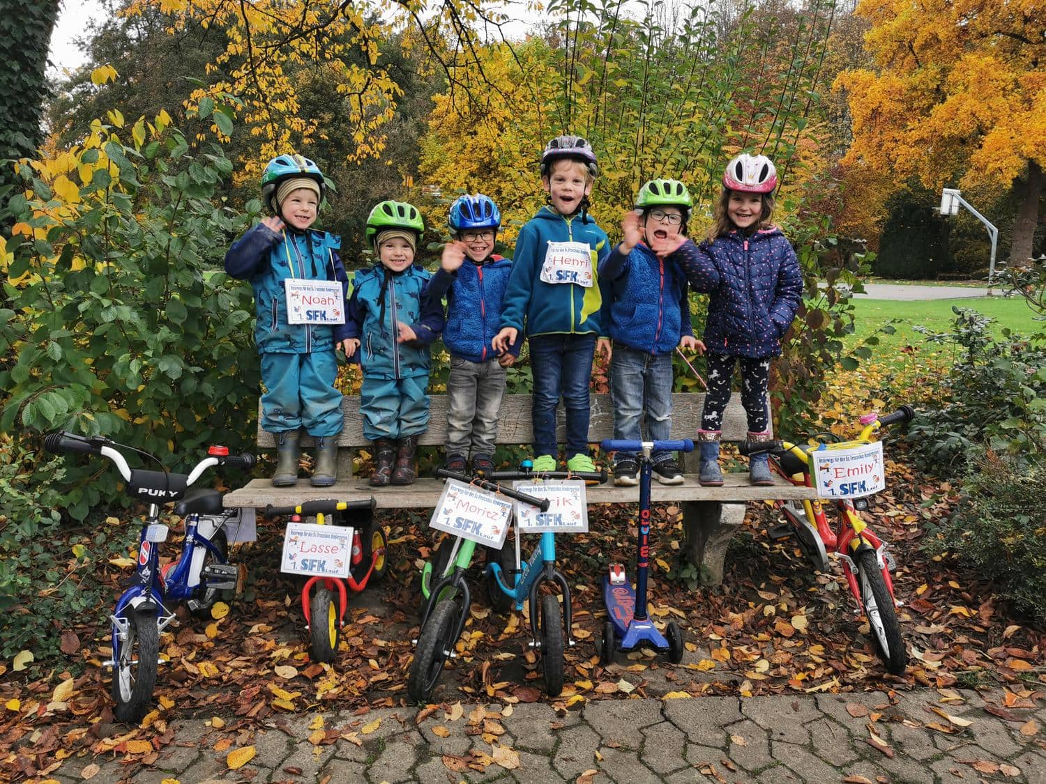 Lachende Kinder mit Fahrradhelmen stehen auf einer Parkbank