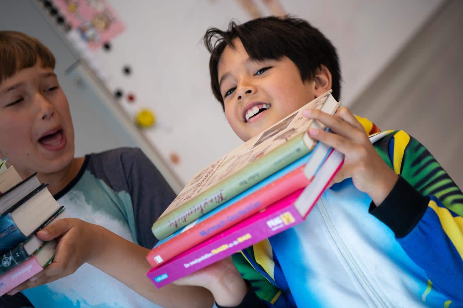 Kinder tragen lachend Buecher in den Haenden