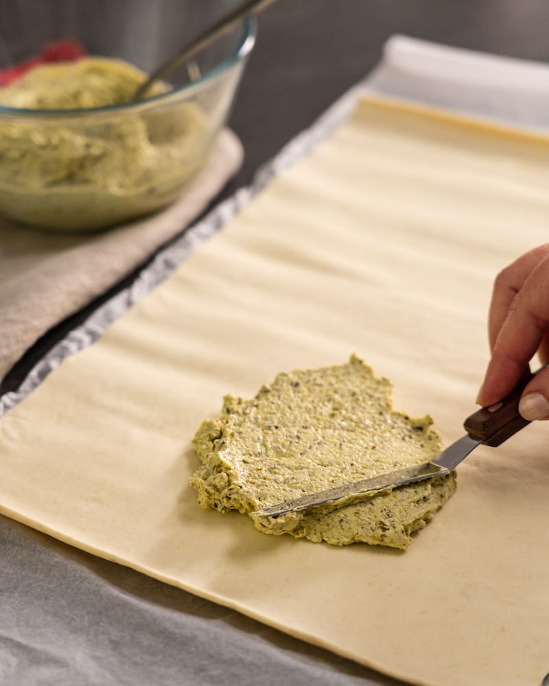 Dieses Bild zeigt wie das Pesto auf den Blätterteig gegeben wird.
