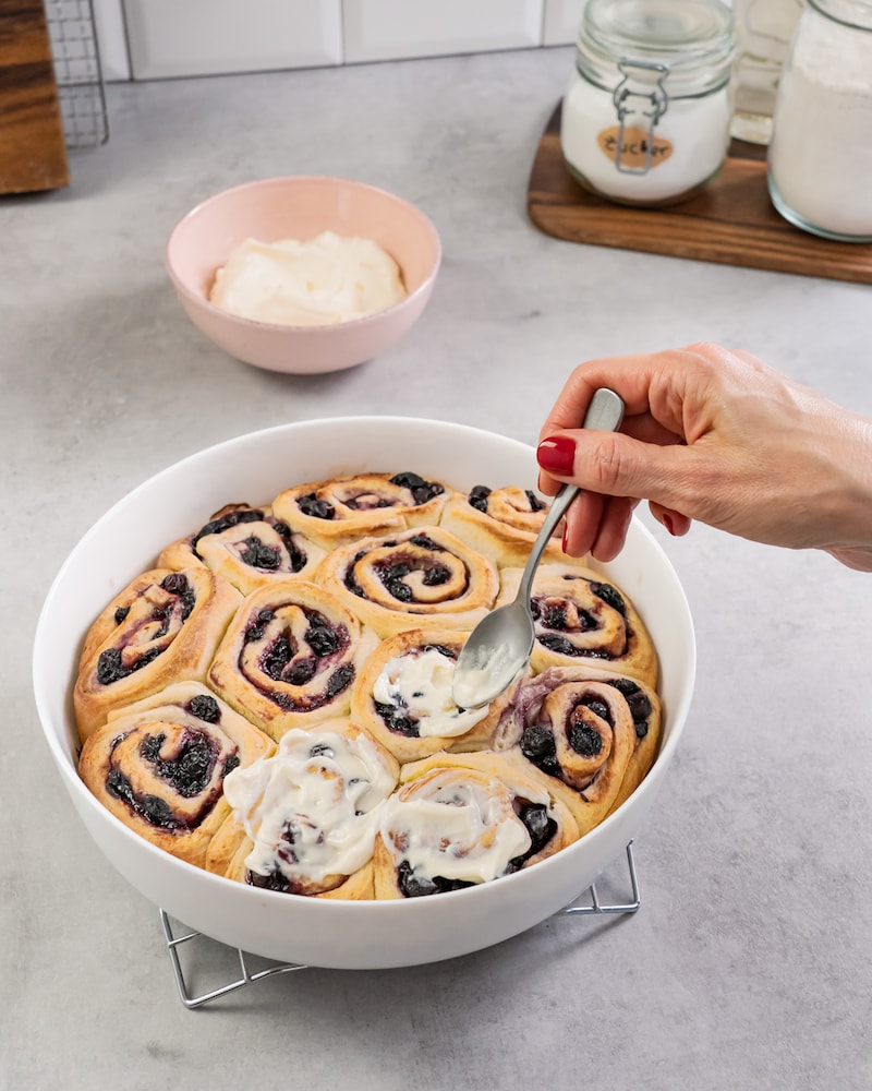 Dieses Bild zeigt wie die fertigen Schnecken mit Zuckerguss bestrichen werden.