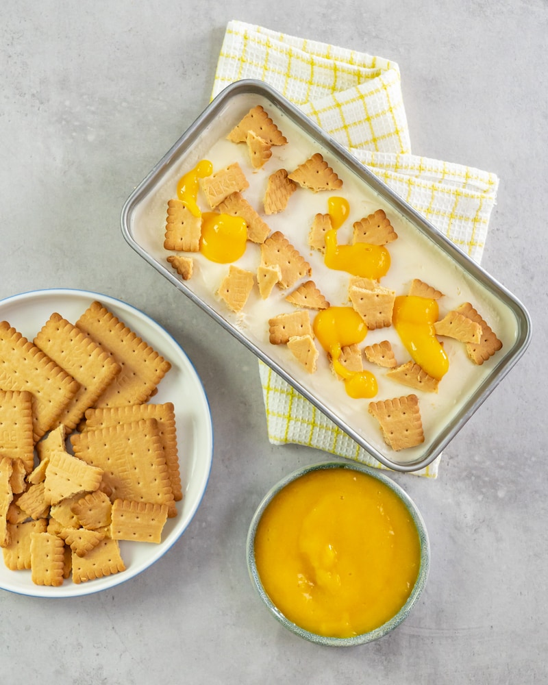 Dieses Bild zeigt wie die Kekse und die Mango auf den Käsekuchen-Eis gegeben wird.