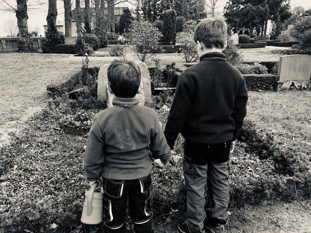 Zwei Kinder stehen Hand in Hand vor einem Grab
