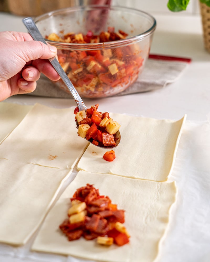 Auf diesem Bild siehst du wie die Käse-Paprika-Mischung auf den Blätterteig gegeben wird.