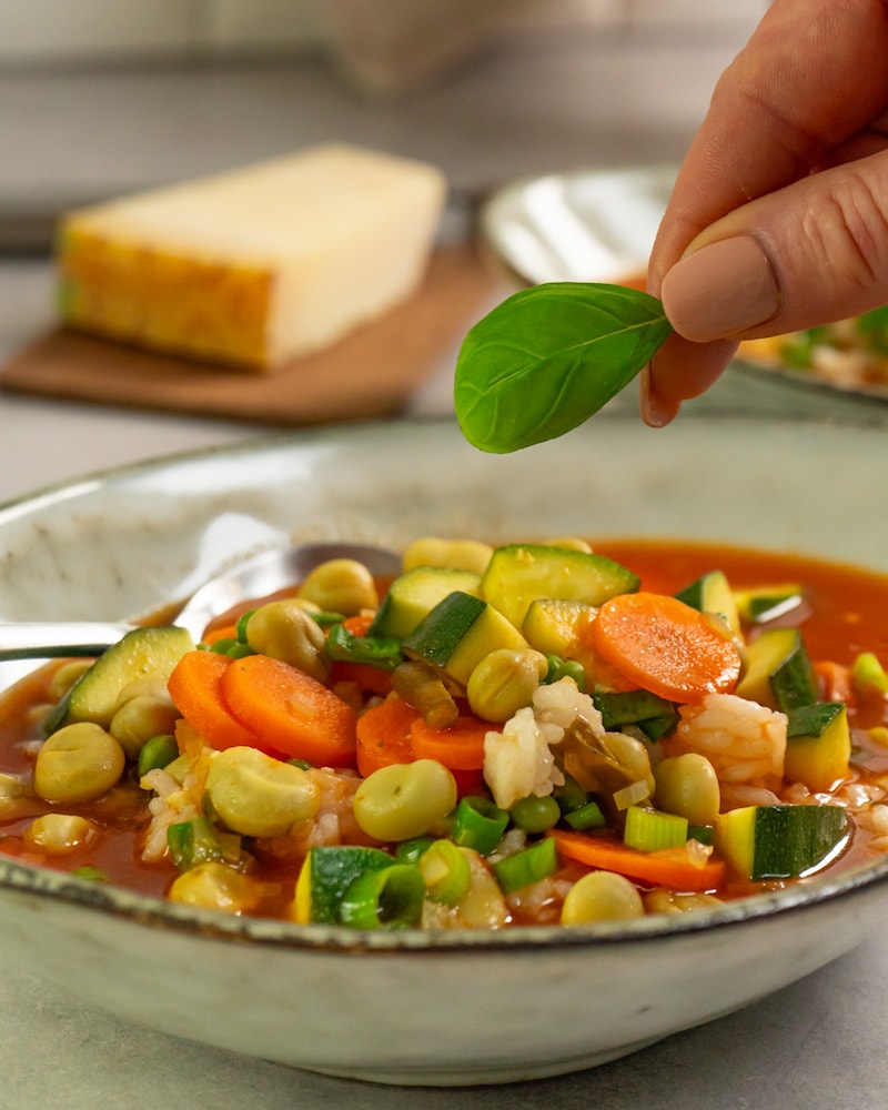 Dieses Bild zeigt die Suppe in die Suppenschale verteilt und mit Basilikum garniert wird.