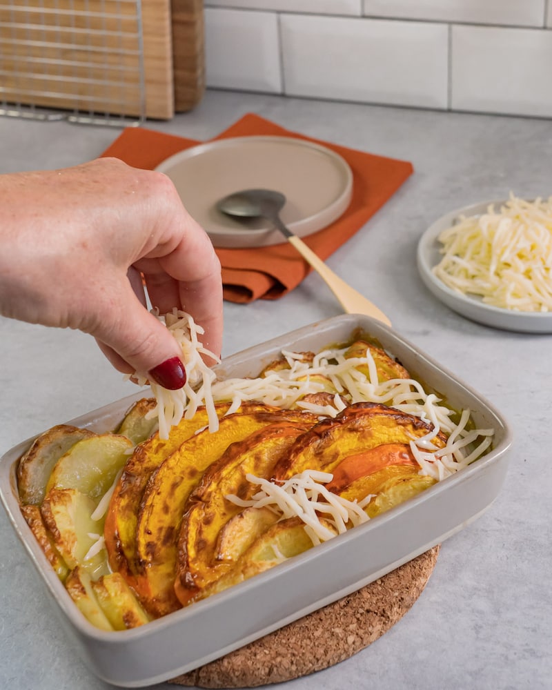 Diese Bild zeigt wie der Käse über den Kürbis und die Kartoffelscheiben gegeben wird.