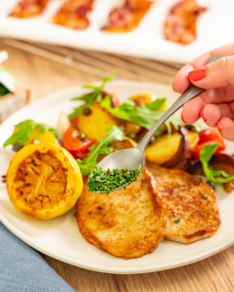 Dieses Bild zeigt wie die 6-Kräuter-Mischung über das Schnitzel gegeben wird.