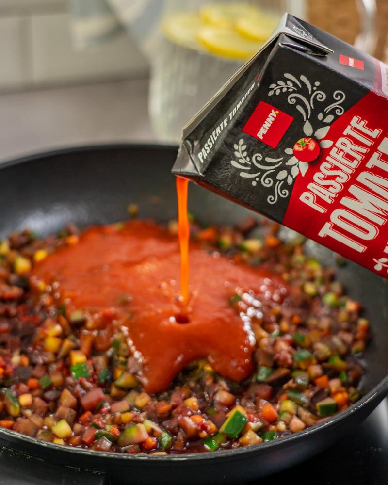 Dieses Bild zeigt, wie die passierten Tomaten ins Gemüse dazu gegeben werden.