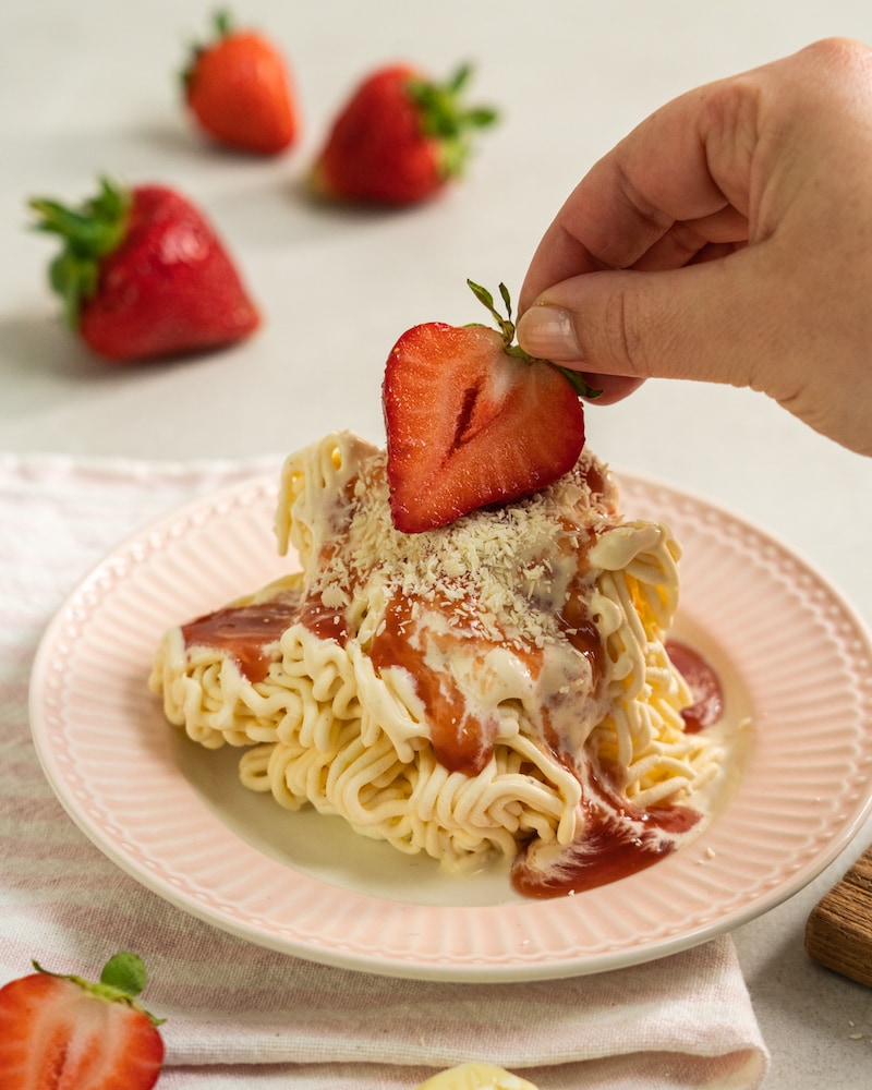 Auf diesem Bild siehst du wie das Eis mit einer Erdbeere garniert wird.